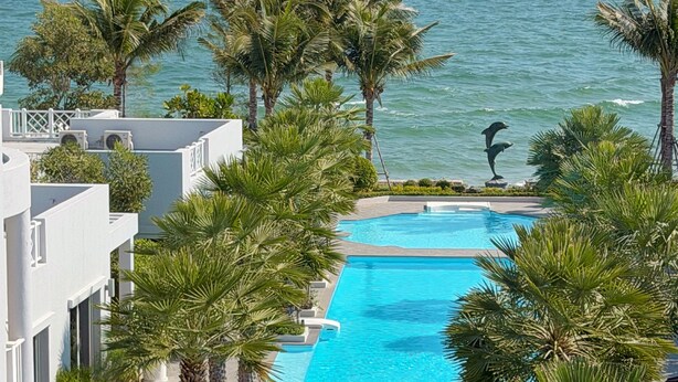 Ein Hotelpool mit Blick auf den Ozean, umgeben von Palmen und einem weißen Gebäude.
