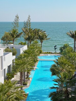 Ein Hotelpool mit Blick auf den Ozean, umgeben von Palmen und einem weißen Gebäude.
