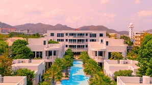Ein Resort mit einem zentralen Pool, umrahmt von weißen Gebäuden, Palmen und einer Bergkulisse.