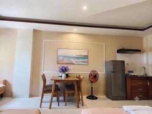 Une pièce comprenant une table à manger, des chaises, un ventilateur, un réfrigérateur et un tableau accroché au mur.