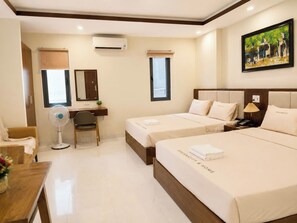 A hotel room with two beds, a desk, a chair, an air conditioner, a window, and a painting on the wall. - New Era Hotel & Apartments (Da Nang)