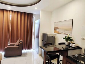 A modern living room with a sofa, a dining table with chairs, a refrigerator, and a painting on the wall. - New Era Hotel & Apartments (Da Nang)