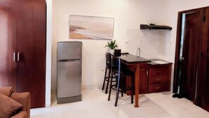 A compact kitchen with a refrigerator, a dining table with chairs, and a hanging light fixture. - New Era Hotel & Apartments (Da Nang)
