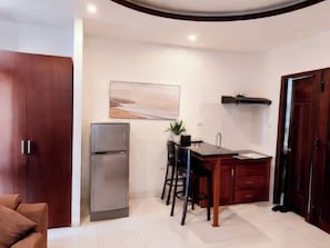 Una cocina compacta con refrigerador, una mesa de comedor con sillas y una lámpara colgante.