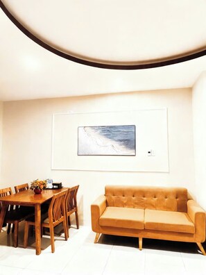 A modern living room with a wooden dining table, a sofa, and a framed artwork on the wall. - New Era Hotel & Apartments (Da Nang)
