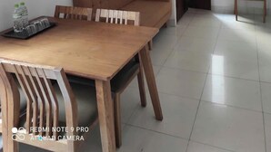 Een woonkamer met een bank, een houten eettafel, een televisie en een ventilator.