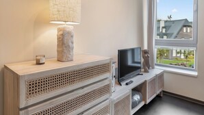 Ein modernes Wohnzimmer mit Fernseher, Lampe und Blick auf ein Haus durch ein Fenster.