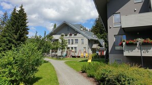 Ein Wohngebäude mit Satteldach, mehreren Fenstern und einem Weg zu einem Spielplatz.
