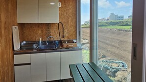 Una cocina pequeña con un lavamanos, armarios de madera y vistas a un campo a través de un ventanal.