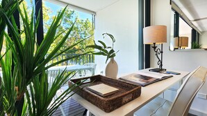 A modern room with a desk, a lamp, a mirror, and a large window with a view of trees. - Sunlit & Peaceful Contemporary Apartment (Randwick)