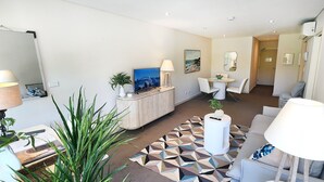 A modern living room with a sofa, a coffee table, a TV, and a dining area with chairs and a table. - Sunlit & Peaceful Contemporary Apartment (Randwick)