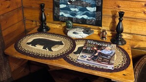 Interieur van een houten blokhut, met een houten tafel waarop een boek, een eendbeeldje en een geweven onderzetter staan.
