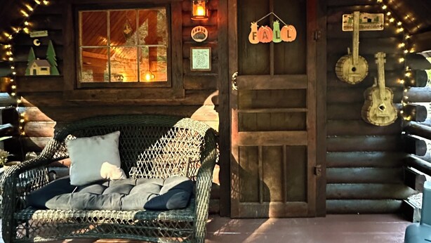 Een gezellig blokhut met een veranda, een rieten stoel, een houten deur en lichtjes.