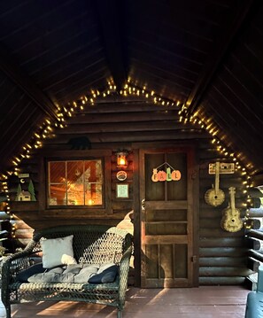 A cozy log cabin with a porch, a wicker chair, a wooden door, and string lights.