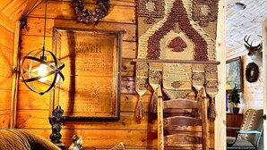 Een gezellig interieur van een blokhut met houten wanden, een ingelijst document, een geweven wandkleed, een hertenkop en een rustieke stoel.