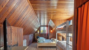 Un dormitorio acogedor en el ático con paredes de madera y techo inclinado. Cuenta con una cama literera, un escritorio y una silla.