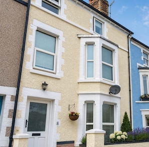 A row of terraced houses with bay windows, a front door, and a hanging flower basket.