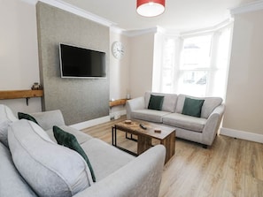 A living room with a grey sofa, a wooden coffee table, a grey couch, and a mounted TV.