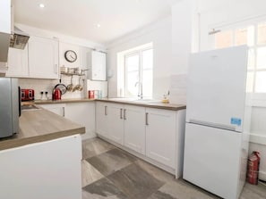 Une cuisine moderne avec des meubles blancs, une hotte de cuisinière en acier inoxydable, une bouilloire rouge et un réfrigérateur blanc.