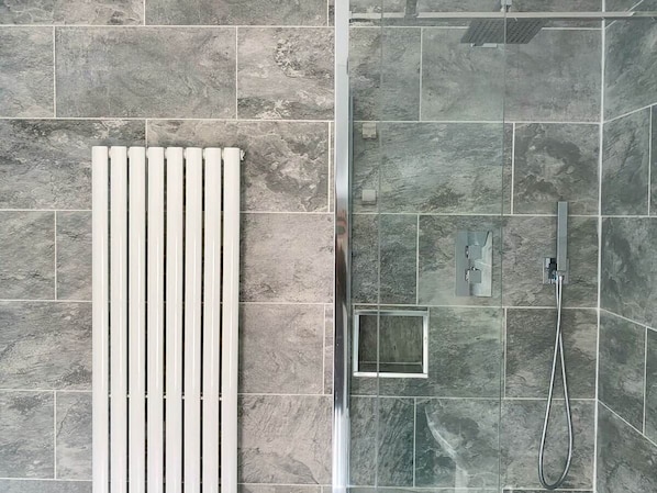 A shower area with a glass enclosure, a white towel rack, and a showerhead.