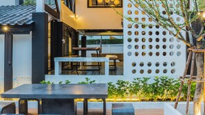 A modern outdoor dining area with a table and benches, surrounded by a white wall with circular cutouts and a tree.