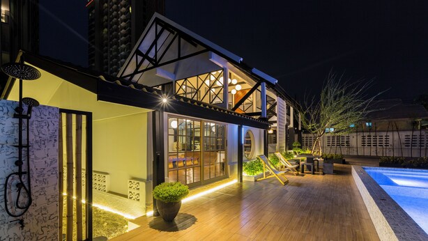 A modern house with a wooden deck, a swimming pool, and a well-lit entrance.