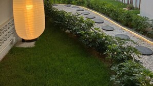 A garden pathway with lanterns, a small pond, and a view of a tall building in the background.