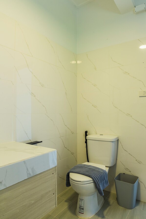 Un baño con inodoro, un cubo de basura y una pared con azulejos de mármol.