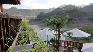 A terrace with outdoor seating, a pool, and a view of a lake and hills.