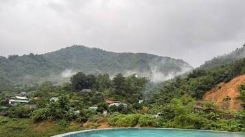 Una piscina rodeada de exuberante vegetación y montañas al fondo.