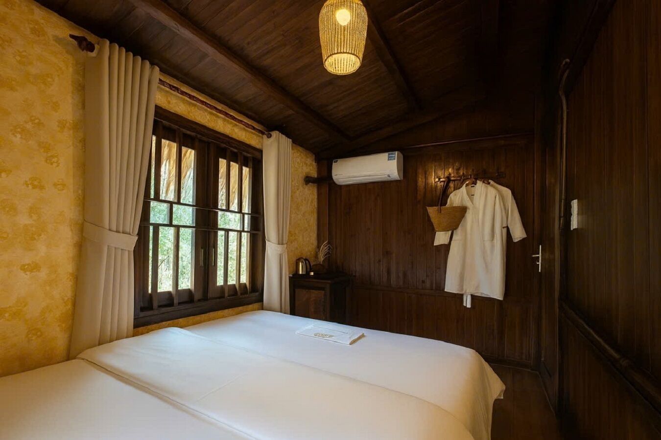 A room with a bed, a window with curtains, an air conditioning unit, and a wooden wardrobe.