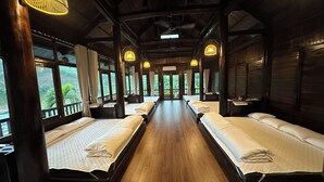 A cabin-style room with wooden floors and walls, large windows, and multiple beds.