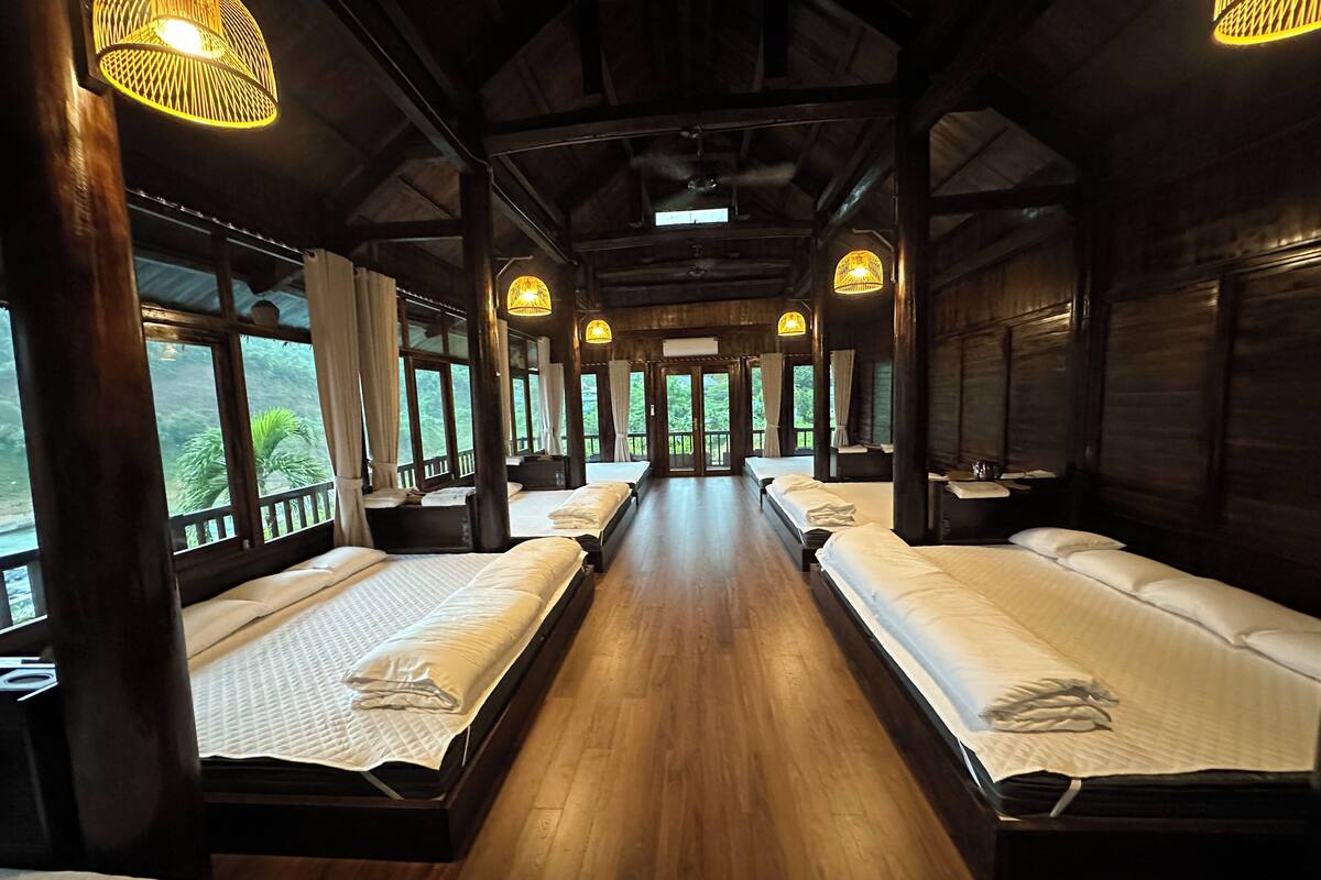 A cabin-style room with wooden floors and walls, large windows, and multiple beds.