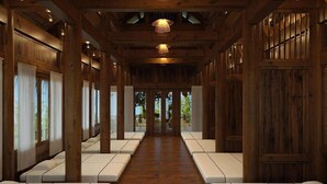 A wooden interior with a central pathway leading to an outdoor area, featuring benches and hanging lights.