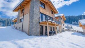 A two-story chalet with a stone facade, wooden balconies, and a snow-covered roof.