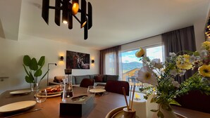 A dining area with a table set for two, a painting on the wall, and a view of the outdoors.