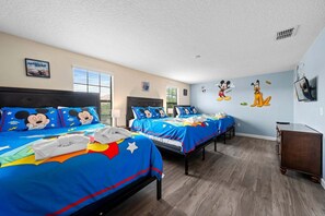 Une chambre d’hôtel avec deux lits, chacun agrémenté de draps à l’effigie de Mickey Mouse, une grande fenêtre et un autocollant mural représentant Mickey Mouse.