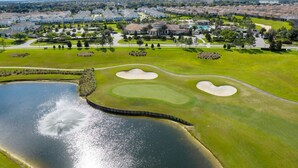 An aerial view of a golf course with sand bunkers, a pond, and surrounding residential areas. - Resort Stay w/ Pool & Amazing Amenities (Davenport)