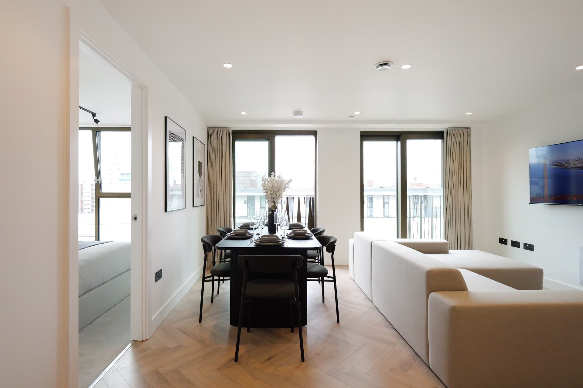 A modern living room with a dining area, large windows, and a flat-screen TV.