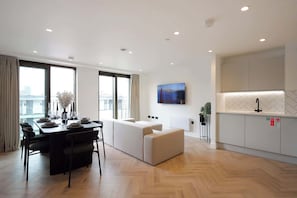 A modern hotel room with a dining area, a sofa, a TV, and a kitchen.