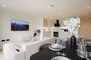 A modern living room with a flat-screen TV, a sofa, a dining table set with plates, glasses, and cutlery.
