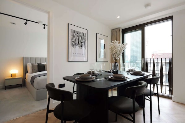 A modern dining area with a black table set for six, a grey sofa, and a city view through large windows.