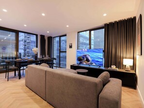 A modern living room with a sofa, a dining table set for four, a flat-screen TV, and a lamp.