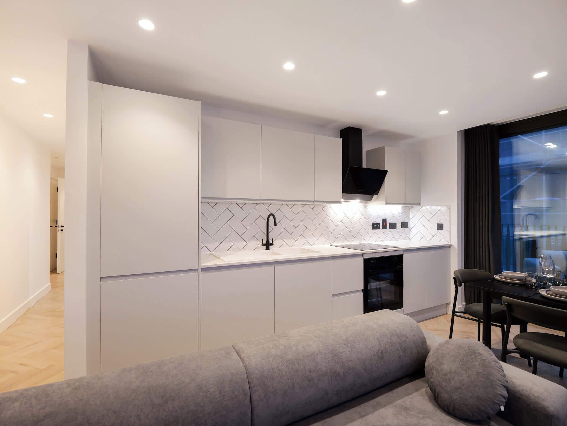 A modern kitchen with white cabinetry, a black faucet, and a herringbone tile backsplash.