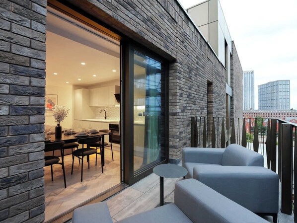 Eine moderne Wohnung mit einer Stein-Fassade, einem Balkon mit Sitzgelegenheit und Blick auf die Stadtlandschaft.