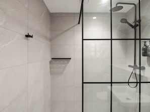 A modern shower area with a glass partition, a handheld showerhead, and a wall-mounted faucet.