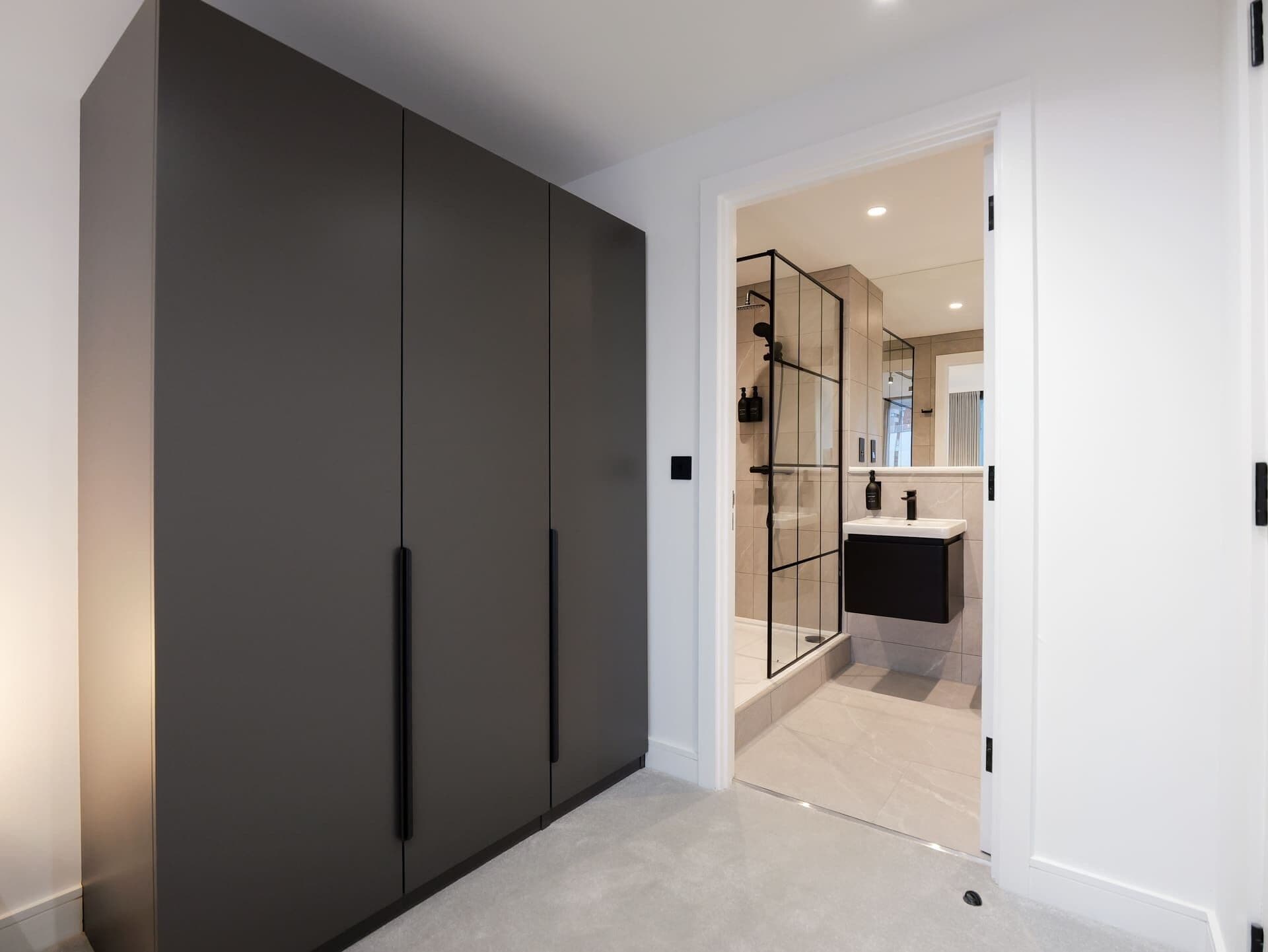 A modern bathroom with a glass shower enclosure, a white sink, and a dark wardrobe.