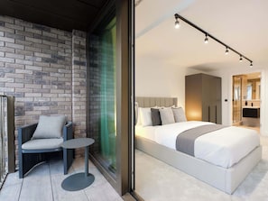 A modern bedroom with a large bed, a chair, a small table, and a brick wall.