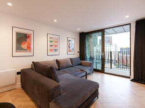 A modern living room with a sofa, a coffee table, and a balcony with a city view. - Solaro | The Heim (Greater Manchester)