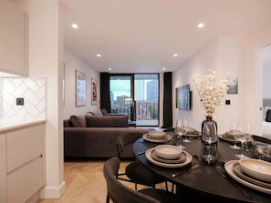 A modern living space with a dining area, sofa, and a balcony with a city view.